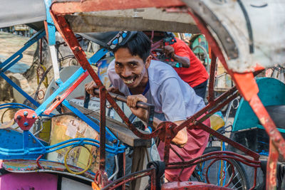 Portrait of smiling man standing amidst pedicab