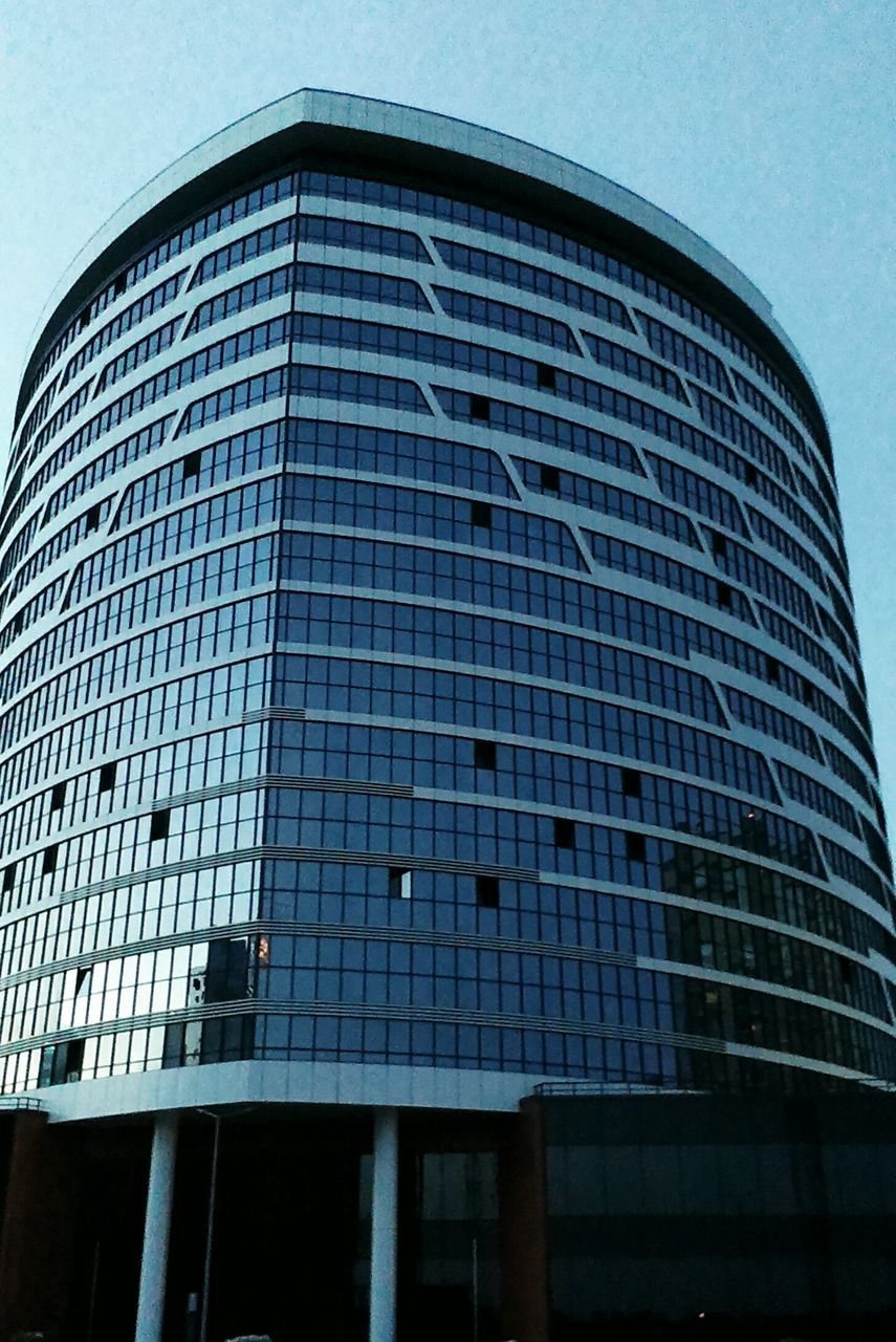 LOW ANGLE VIEW OF MODERN GLASS BUILDING AGAINST BLUE SKY