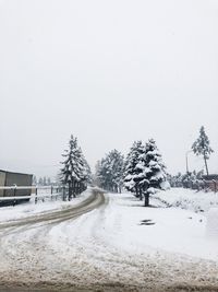 Snow covered field by road against clear sky