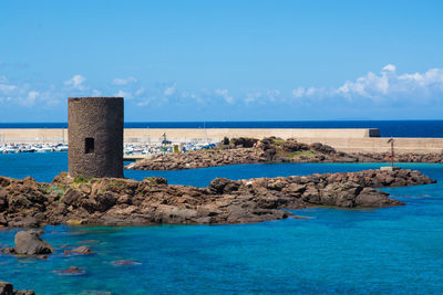 Tower amidst sea against sky at castelsardo