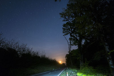 Road amidst trees against sky at night