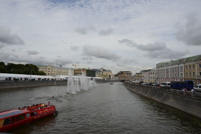 Boats in river by buildings in city against sky