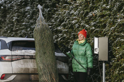 Smiling woman standing with christmas tree near car