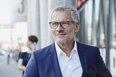 Confident businessman outdoors with woman in background