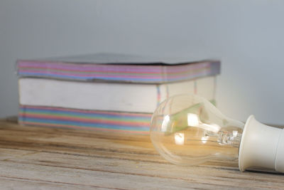 Close-up of light bulb and books on table against wall