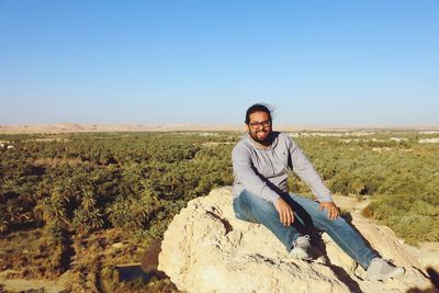 Portrait of man sitting on land against clear sky