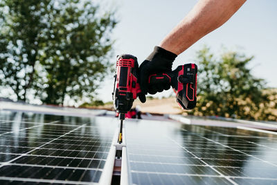 Hand of technician man assembling solar panels with drill on house roof for self consumption energy