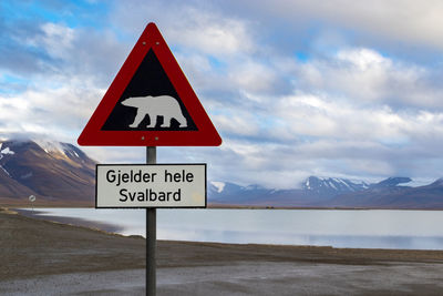 Road sign by snowcapped mountain against sky