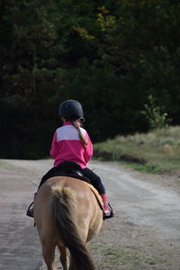 Rear view of girl riding horse on road