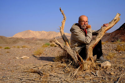 Senior man sitting in the desert against clear sky