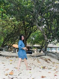 Full length portrait of young woman standing against trees
