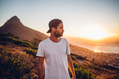 Young man standing on mountain against sky during sunset