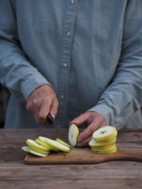 Closeup adult woman hands cutting fresh green apples on wooden cutting board 