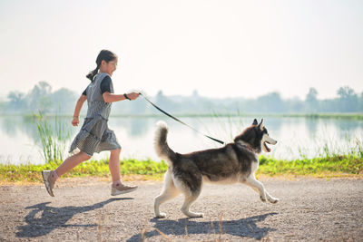 Full length of girl with dog running on road