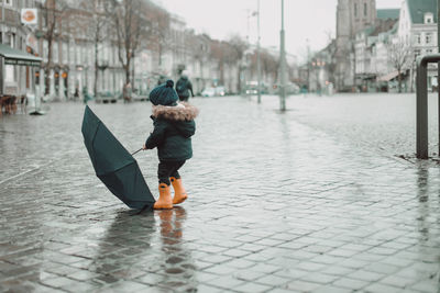 Rear view of woman walking on wet street in rainy season