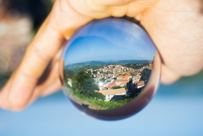 Cropped hand holding crystal ball with reflection of townscape