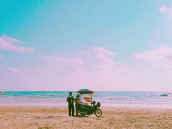 People riding motorcycle on beach against sky