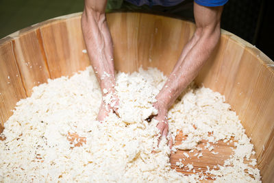 Cropped hands of man crushing cheese in wooden container