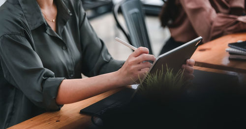 Midsection of woman using mobile phone while sitting on table