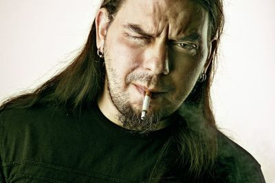 Close-up portrait of man smoking cigarette against white background