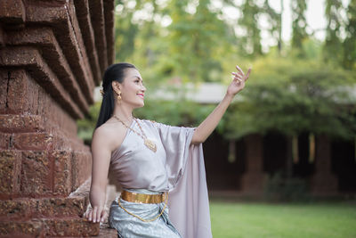 Young woman in traditional clothing looking away while sitting on building wall