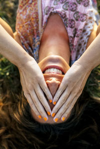 Smiling young woman covering eyes with hands while lying on field