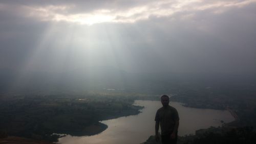 Rear view of man standing on mountain against sky