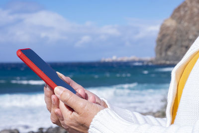 Hand holding smart phone by sea