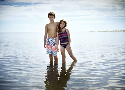Portrait of brother standing with arm around sister on sea shore