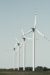 Low angle view of wind turbines on field against clear sky