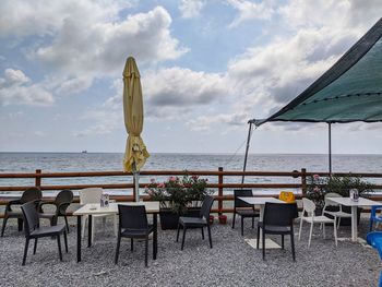 Chairs and tables at beach against sky