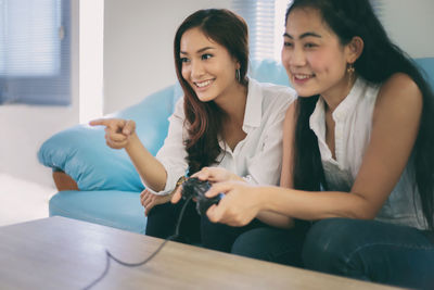 Young women playing video game while sitting on sofa at home
