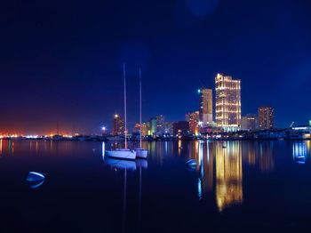 Illuminated buildings by river against sky at night