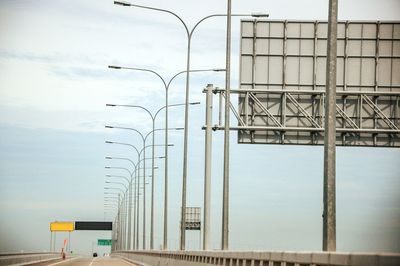 Billboard and street lights on bridge against sky