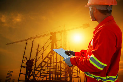 Man working at construction site against sky during sunset