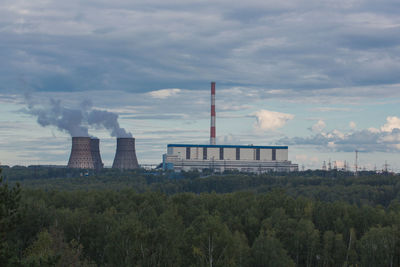 Smoke emitting from factory against cloudy sky