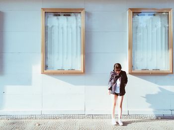 Full length of young woman standing against building on sunny day