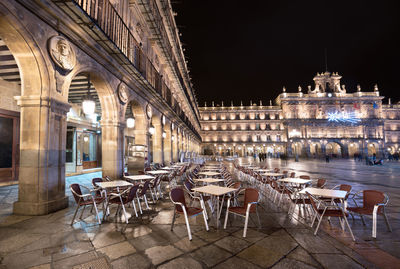 Chairs and tables at sidewalk cafe in city at night