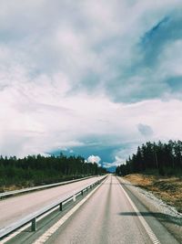 Highway amidst trees against cloudy sky