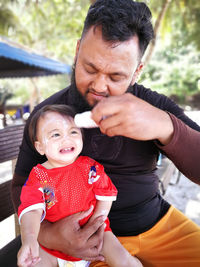 Father holding toy and daughter crying while sitting on bench