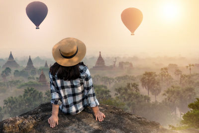 Rear view of young woman sitting on mountain against sky during sunset