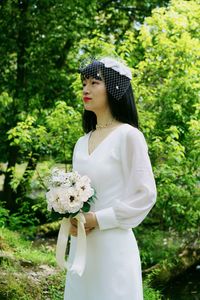 Bride with bouquet standing against trees