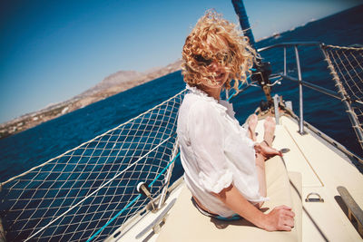 Happy woman with curly hair sitting on boat over sea