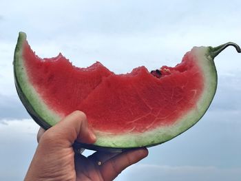 Close-up of hand holding watermelon slice against sky