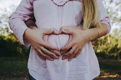 Cropped hands of man making heart shape on pregnant woman abdomen