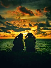 Women sitting by sea against sky during sunset