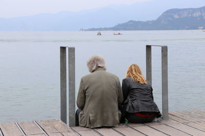 Rear view of people sitting on pier over sea