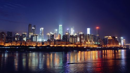 Illuminated cityscape by river against sky at night