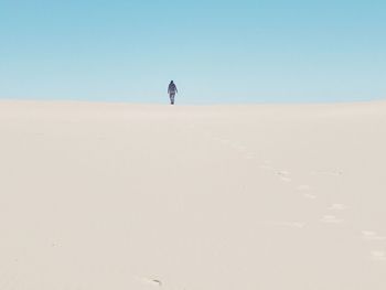 Man walking in desert against clear blue sky