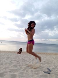 Cheerful woman jumping at beach against sky